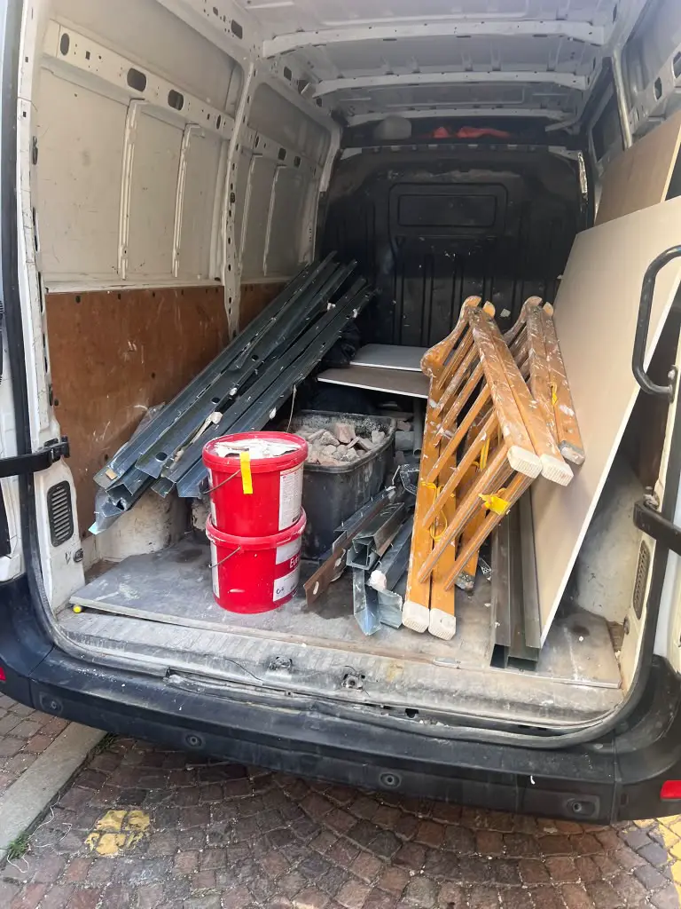 Furgone carico di profili metallici, secchi, scala in legno e cartongesso da un cantiere